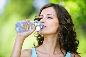 Portrait of young beautiful dark-haired woman wearing blue t-shirt drinking water at summer green park.